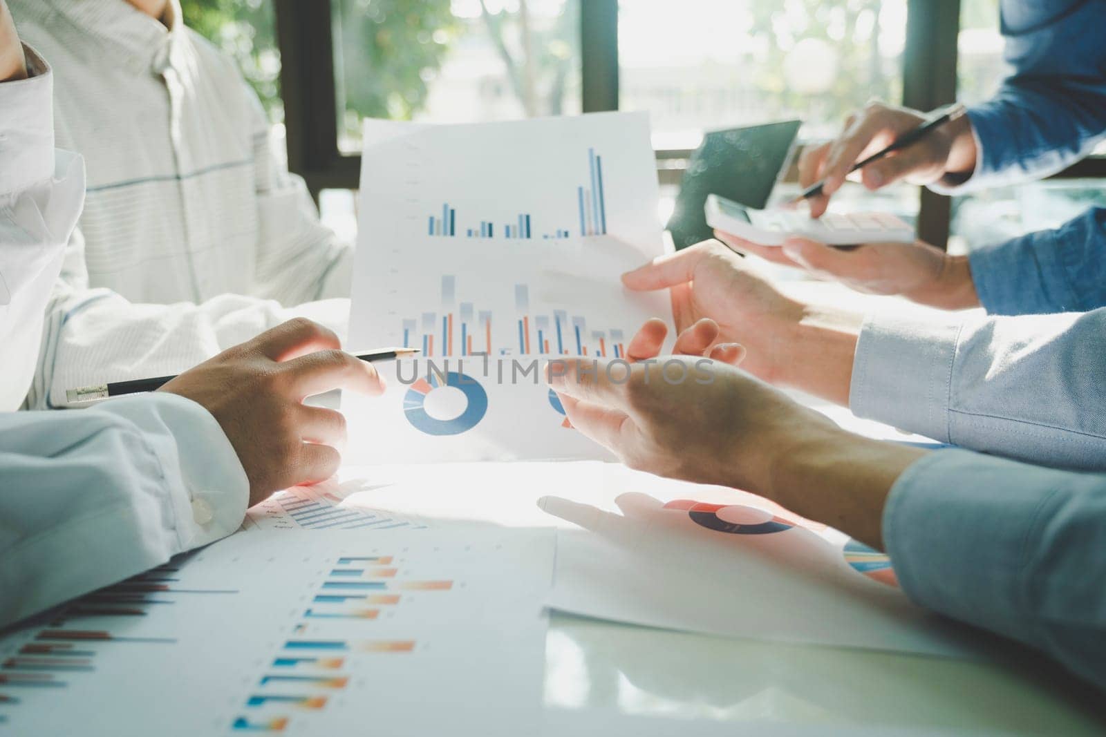 Close-up of businessmen working together at workplace, discussing about strategies, plans, analytic progress, and financial stats, and pointing at graph documents on desk holding pencils and calculator. Business and Teamwork concept.