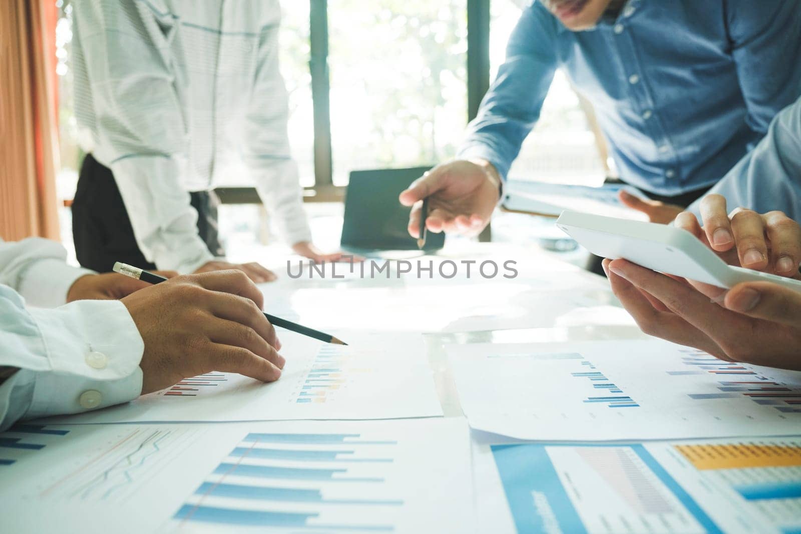 Close-up of businessmen working together at workplace, discussing about strategies, plans, analytic progress, and financial stats, and pointing at graph documents on desk holding pencils clipboard, and calculator. Business and Teamwork concept.
