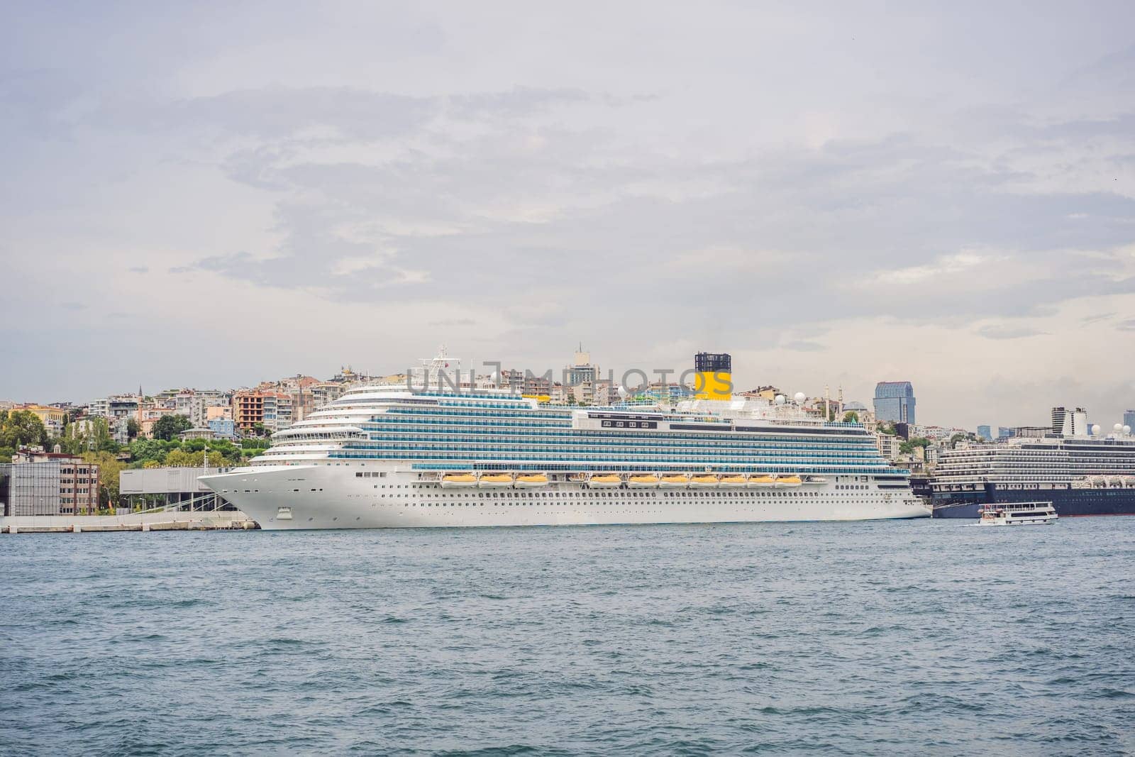 Huge cruise ship docked at terminal of Galataport, located along shore of Bosphorus strait, in Karakoy neighbourhood, with Galata tower in the background.