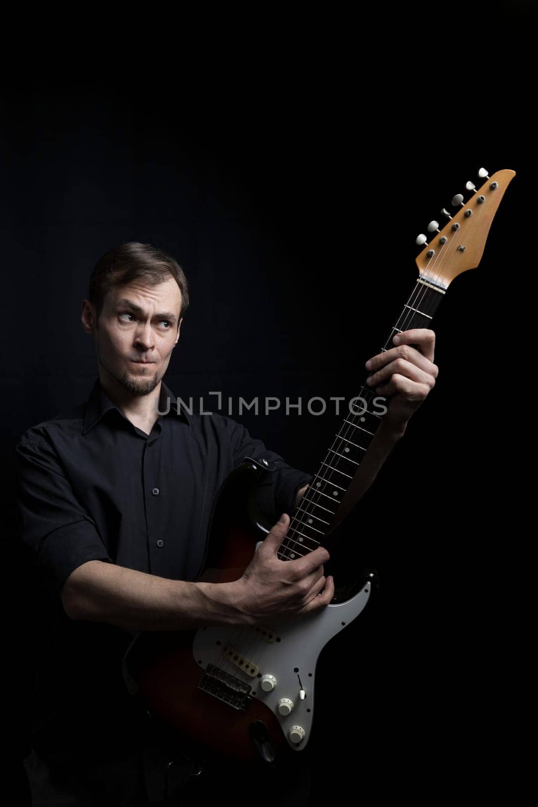 Young caucasian man learning to play electric guitar on black background.