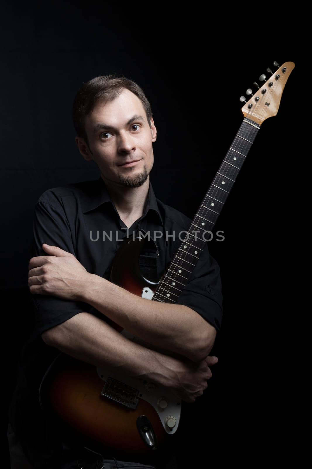 Young man hugging electric guitar look at camera on black background.