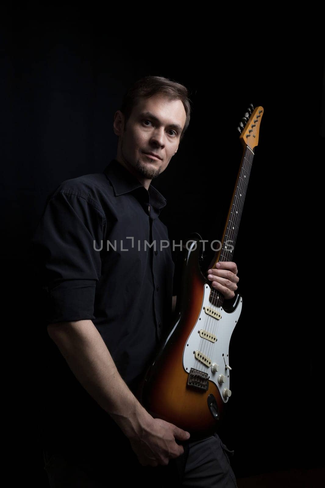 Studio low key portrait of caucasian man with electric guitar with dark lighting.