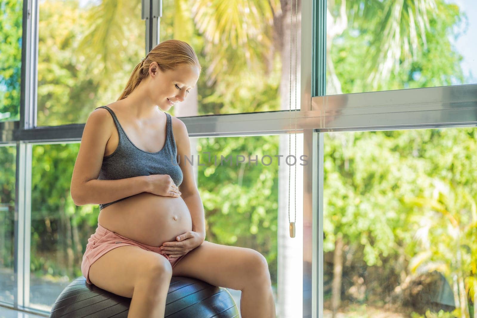 Pregnant woman exercising on fitball at home. Pregnant woman doing relax exercises with a fitness pilates ball. Against the background of the window.