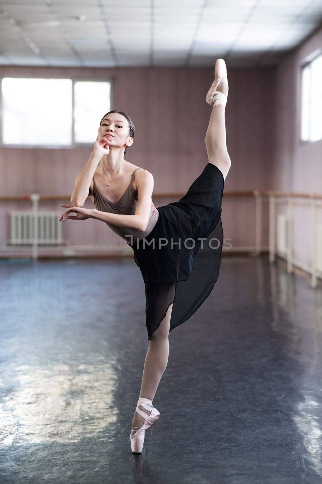 Graceful Asian ballerina in a beige bodysuit and black skirt is rehearsing in a dance class. by mrwed54