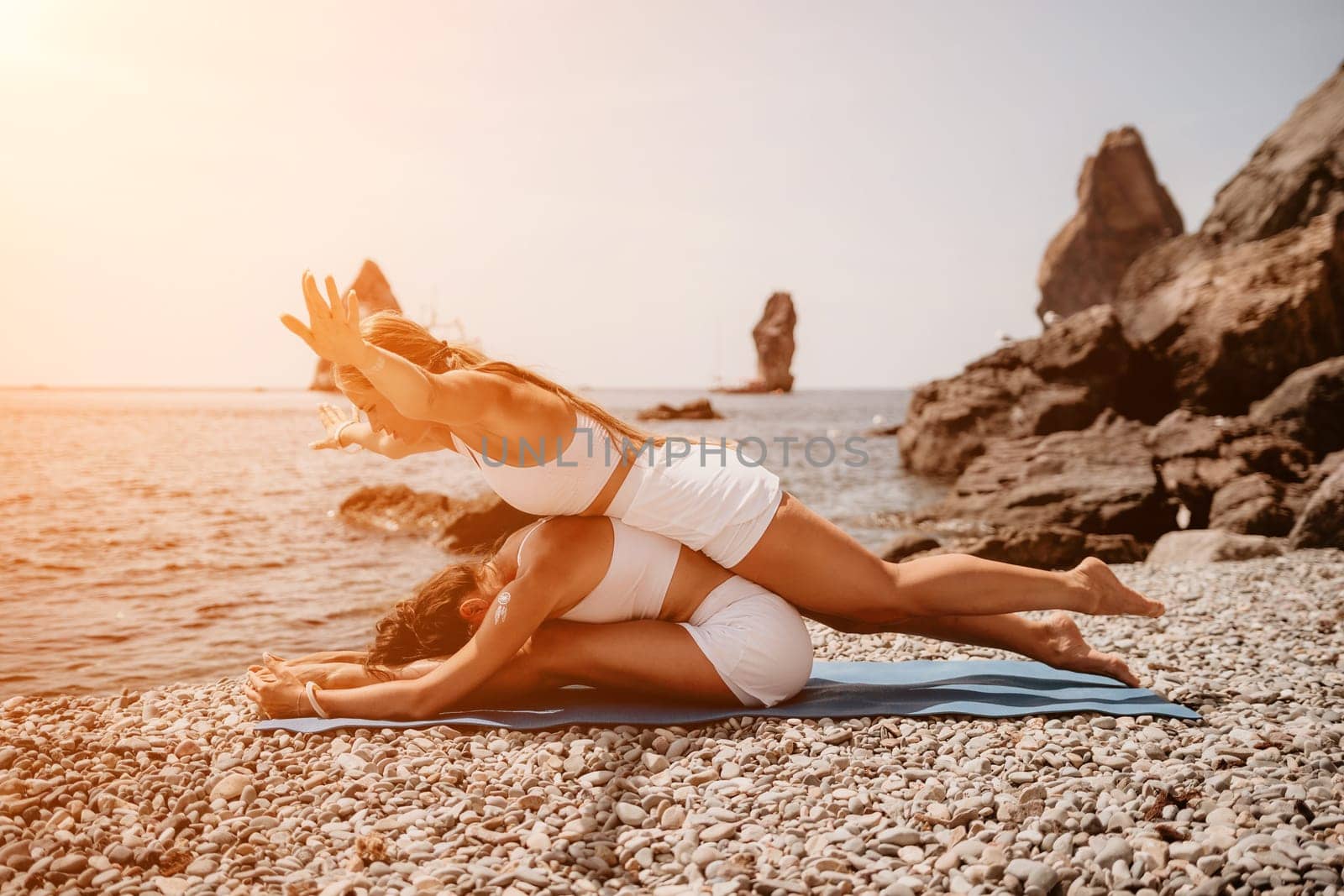 Woman sea yoga. Two Happy women meditating in yoga pose on the beach, ocean and rock mountains. Motivation and inspirational fit and exercising. Healthy lifestyle outdoors in nature, fitness concept. by panophotograph