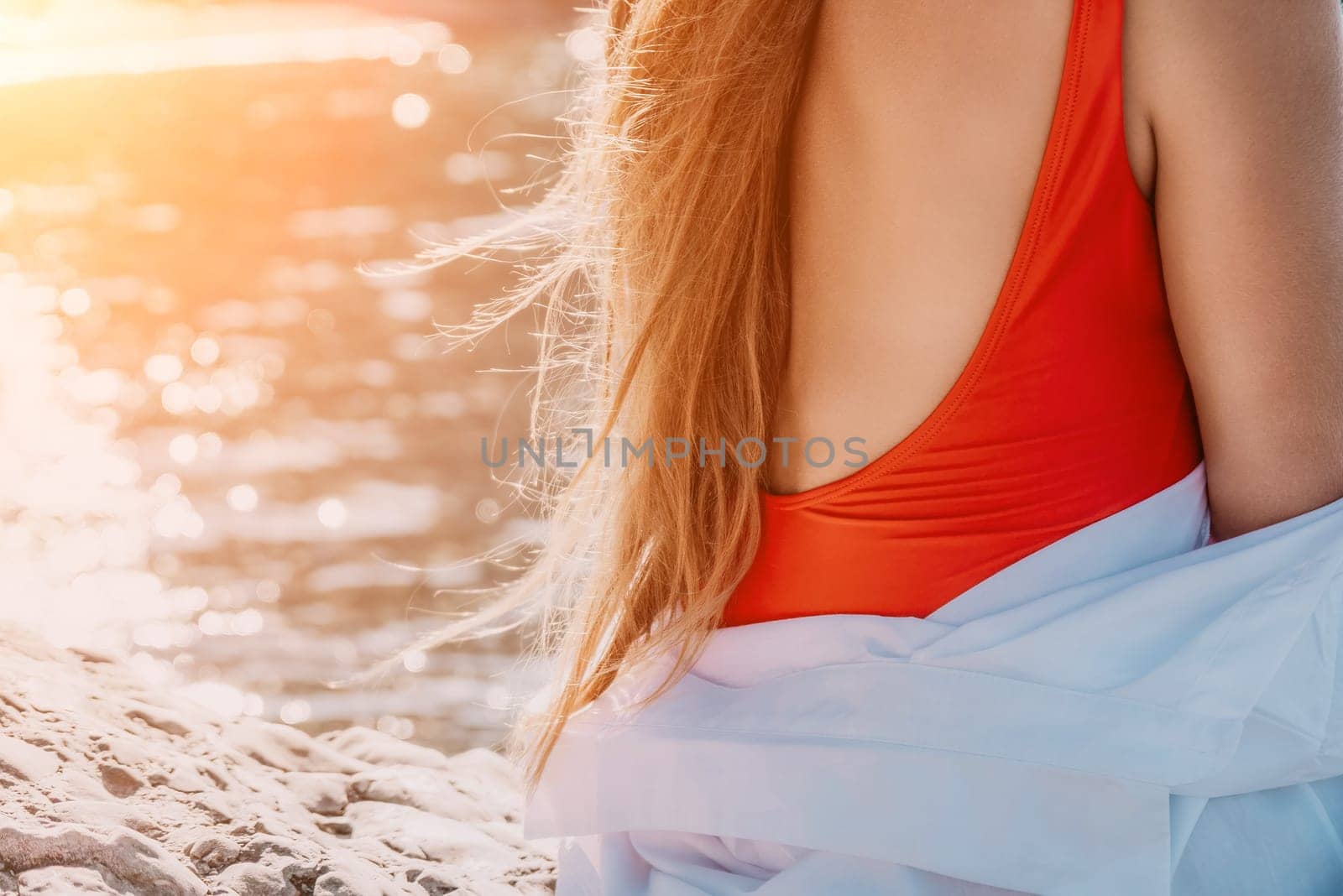 Young woman in red bikini on Beach. Girl lying on pebble beach and enjoying sun. Happy lady in bathing suit chilling and sunbathing by turquoise sea ocean on hot summer day. Close up. Back view by panophotograph