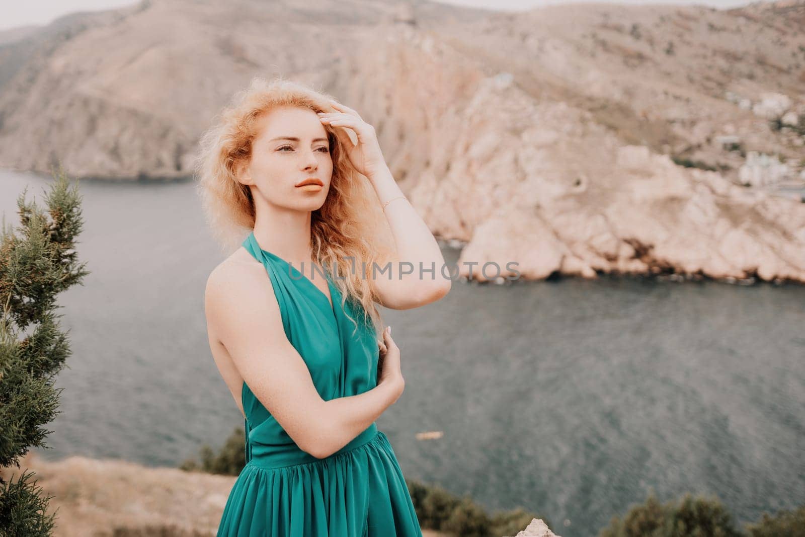 Redhead woman portrait. Curly redhead young caucasian woman with freckles looking at camera and smiling. Close up portrait cute woman in a mint long dress posing on a volcanic rock high above the sea by panophotograph