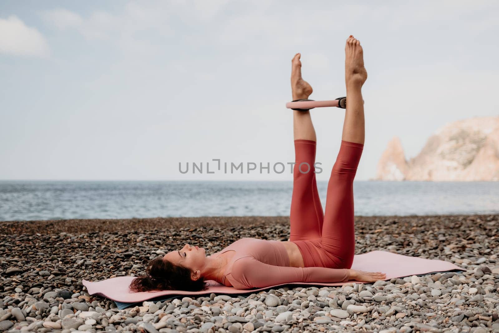 Woman sea pilates. Sporty happy middle aged woman practicing fitness on beach near sea, smiling active female training with ring on yoga mat outside, enjoying healthy lifestyle, harmony and meditation by panophotograph