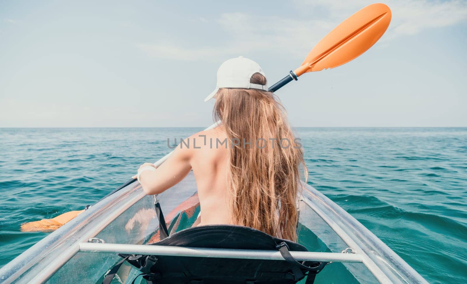 Woman in kayak back view. Happy young woman with long hair floating in transparent kayak on the crystal clear sea. Summer holiday vacation and cheerful female people relaxing having fun on the boat by panophotograph