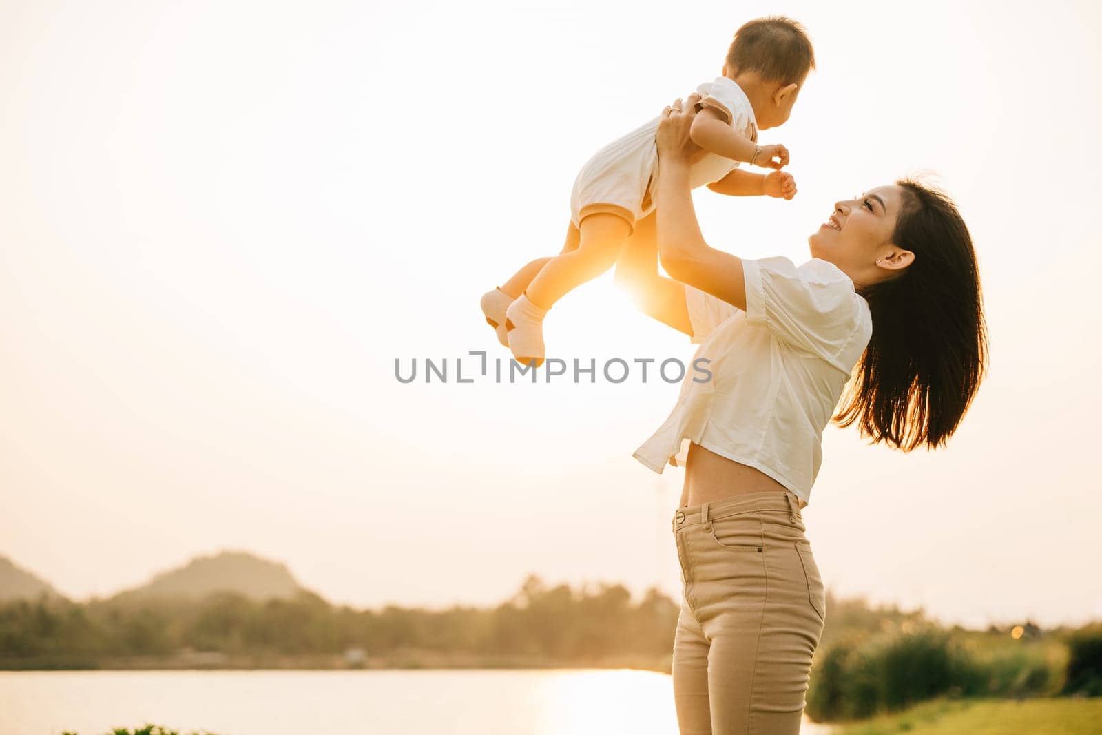 In a carefree summer moment, mom holds her cute toddler son up high, throwing him up into sky. playful child enjoys freedom of flying, while cheerful mother smiles and enjoy moment of family happiness