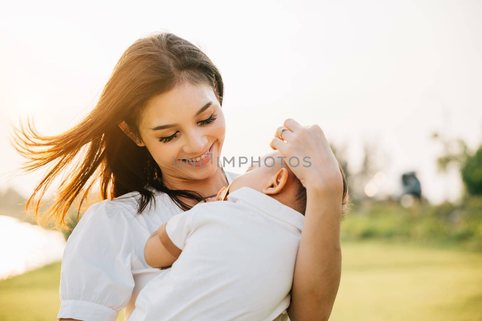 Portrait of a contented mother holding her sleeping son in a serene garden. Her face beams with joy and happiness as she takes in beauty of outdoors with her newborn. A moment of family care and bliss