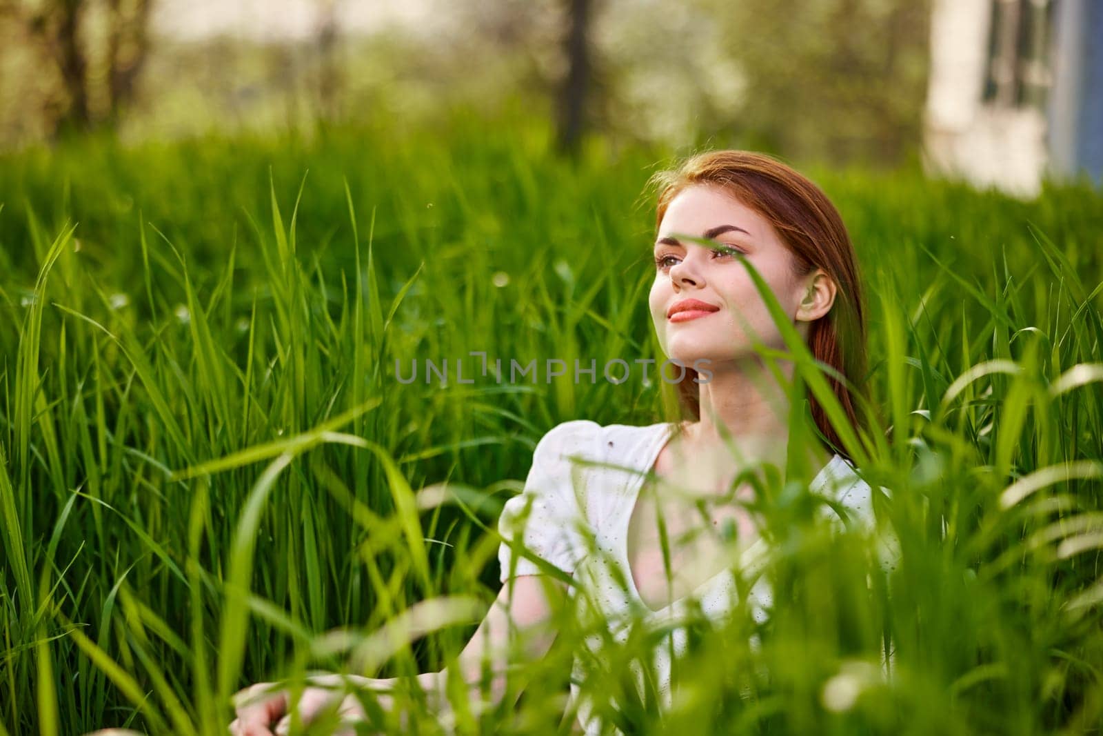 a young woman in a light summer dress enjoys nature sitting in the tall grass by Vichizh