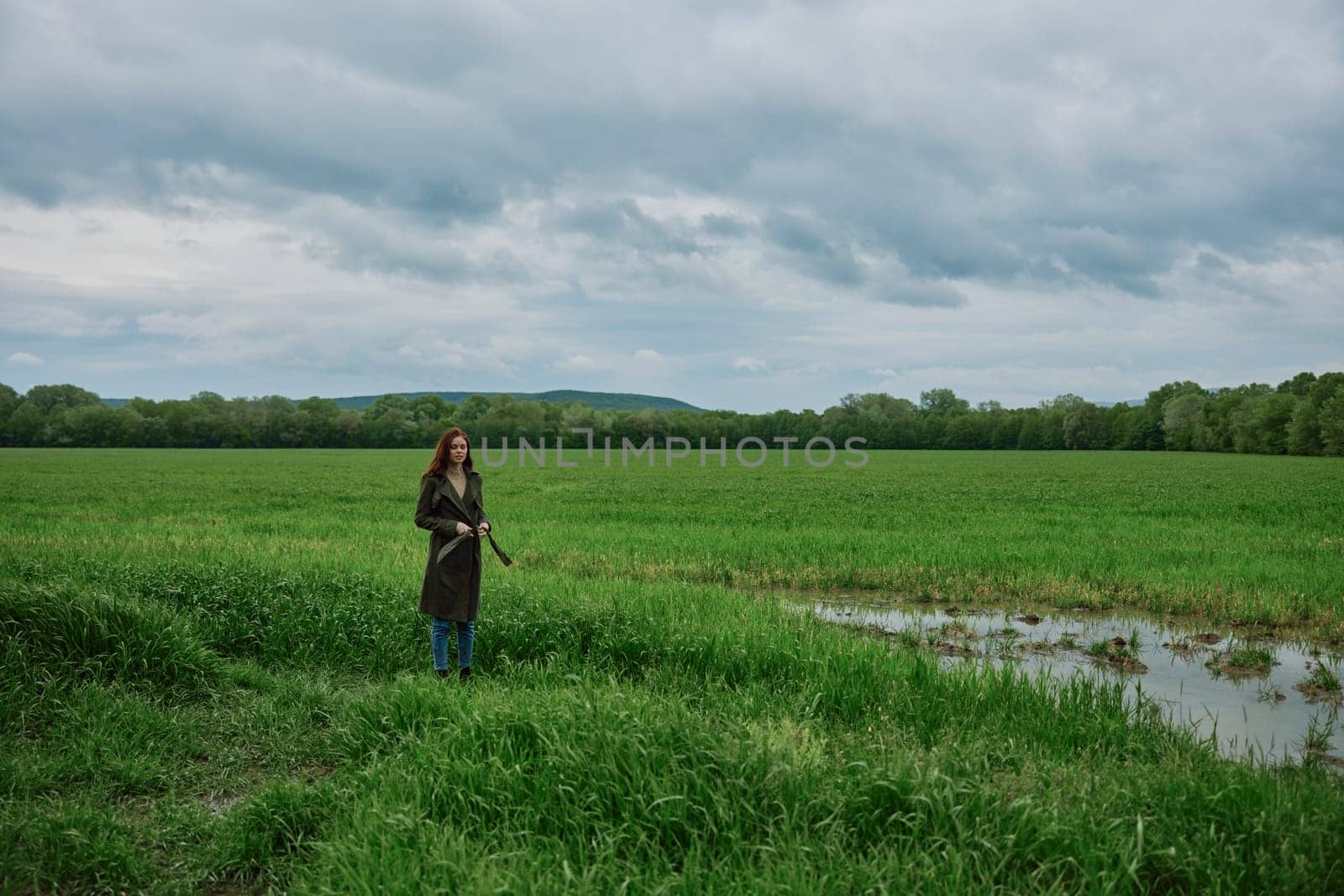 a woman stands in the middle of a green field in warm clothes. Rainy weather, walk in the forest. High quality photo