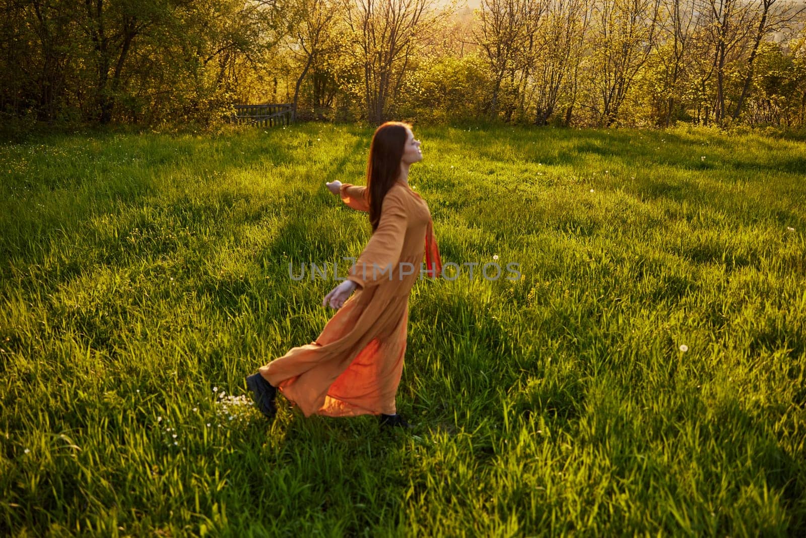 a joyful woman runs through a green field with her hands behind her back, enjoying a warm summer day and nature during the sunset. Horizontal photography in nature. High quality photo