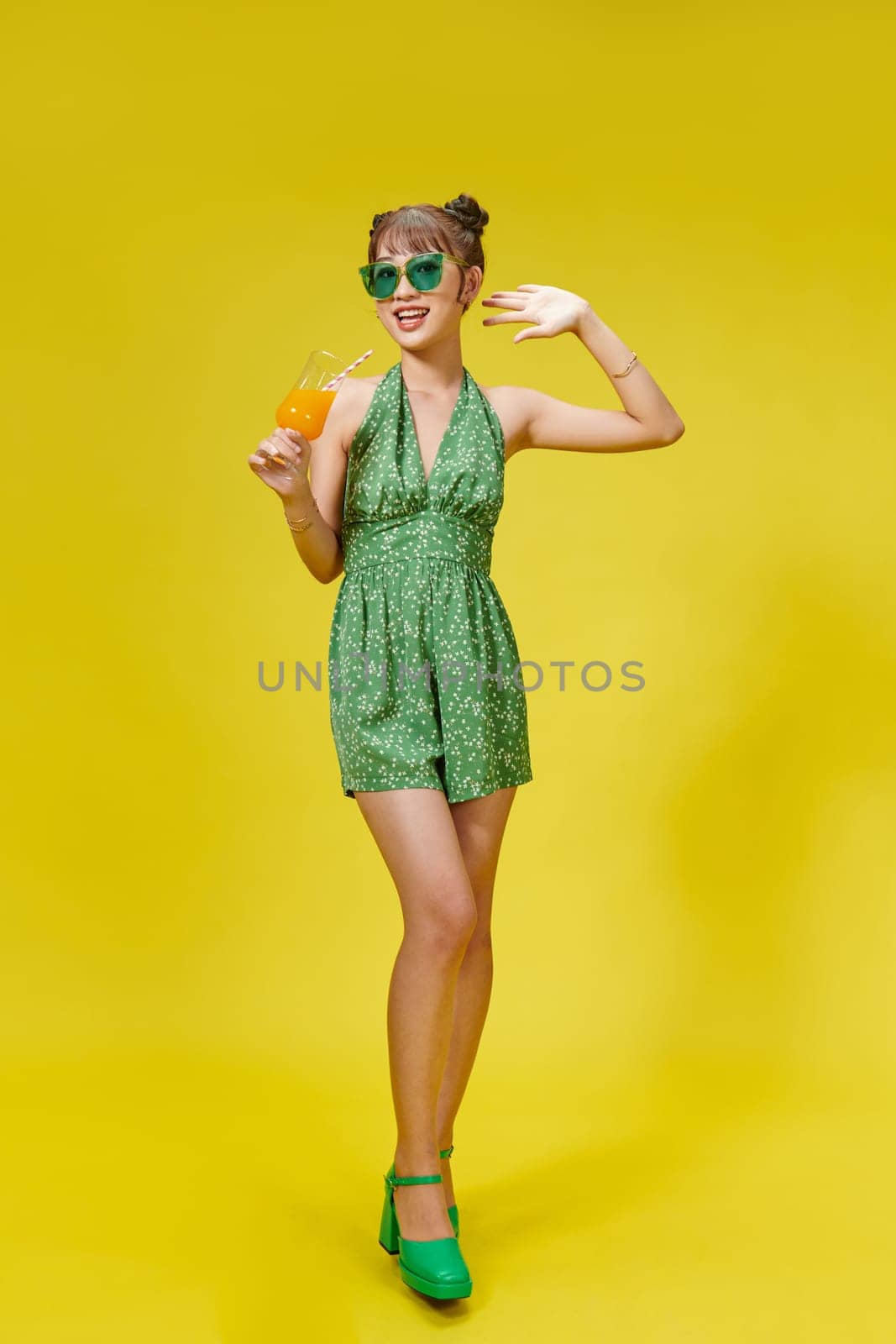 Young woman with sunglasses smiling cheerful and holding a glass of orange juice in summer