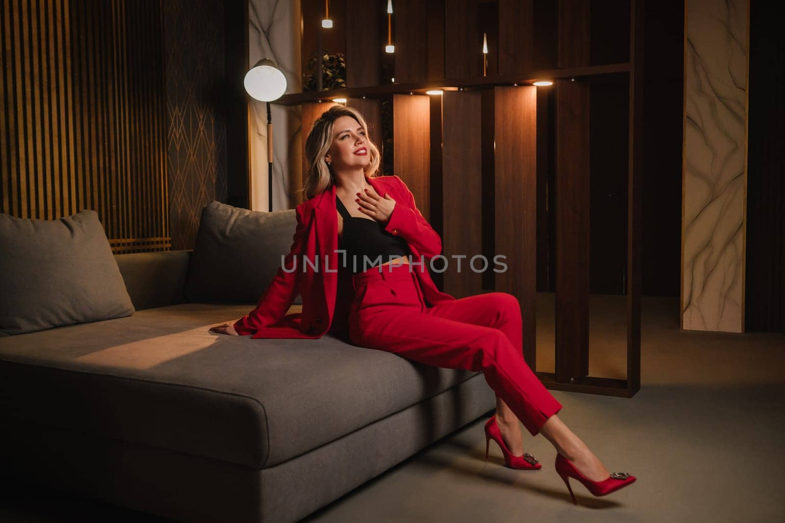 a beautiful girl dressed in a red formal suit posing in a modern interior.