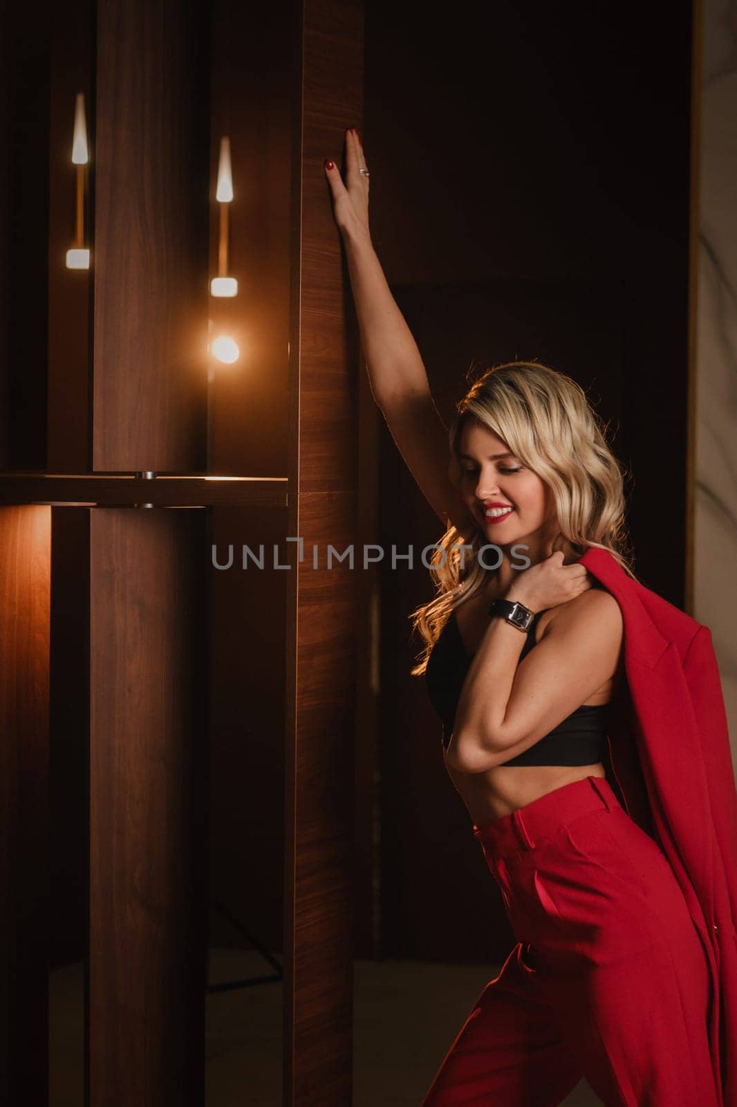 a beautiful girl dressed in a red formal suit posing in a modern interior.