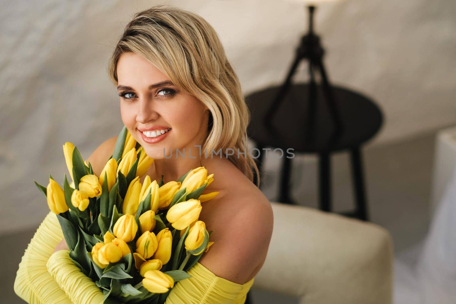 a happy woman in a yellow dress embraces a bouquet of yellow spring tulips in the interior.