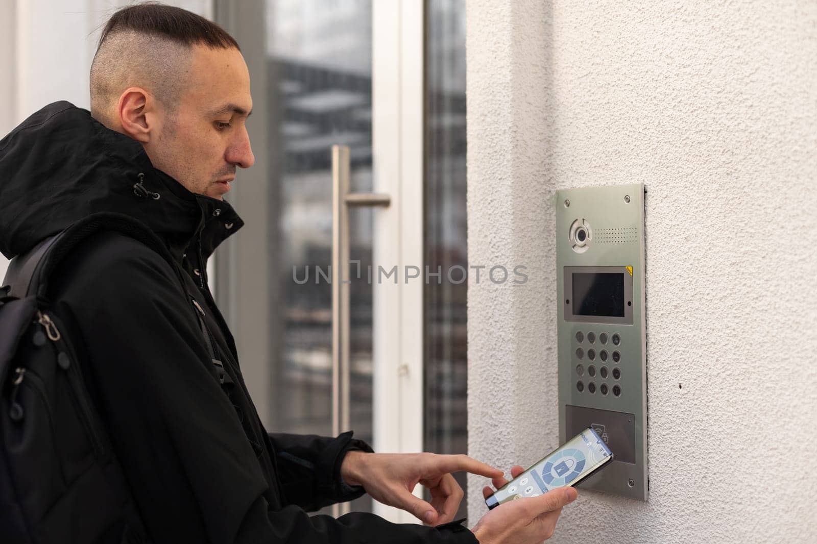 Cut in picture hand of a man turning on the intercom with smartphone outdoor close up. by Andelov13