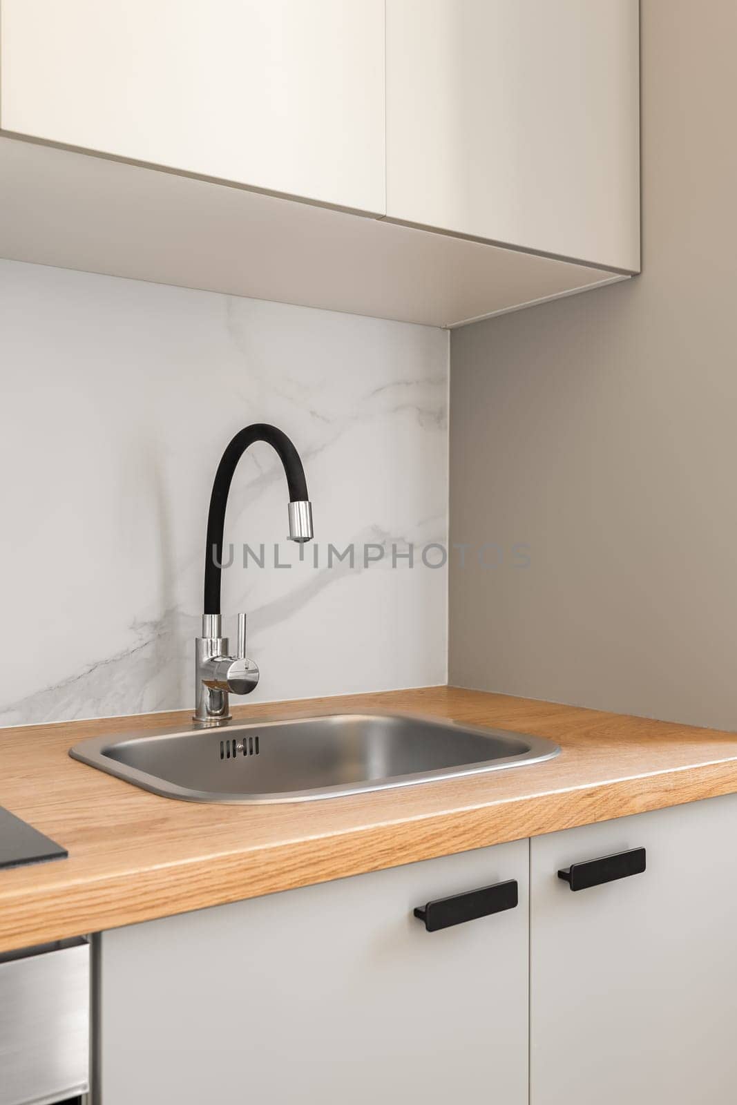 Piece of kitchen in gray solid colors with comfortable wall cabinets and modern fixtures in a new apartment. The concept of repair after the delivery of a new building. Copyspace.
