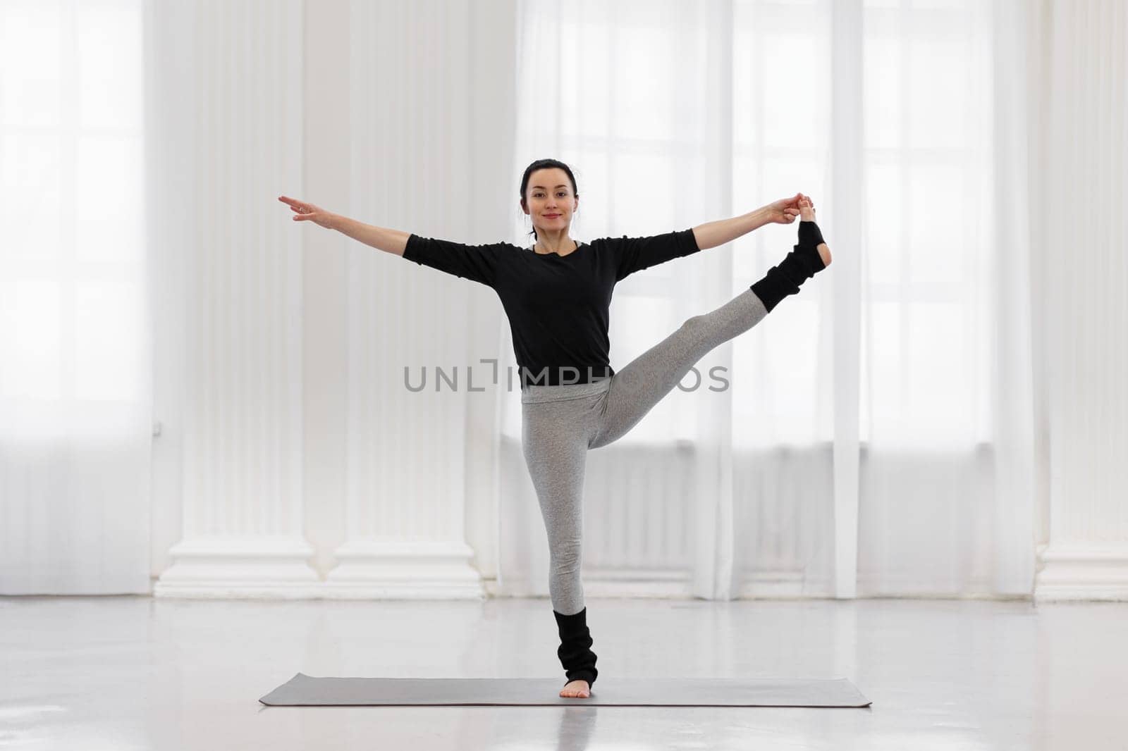 Cheerful young woman doing utthita hasta padagusthasana in the gym while yoga classes. Concept of flexibility, leg and back muscle tone, balance and concentration.