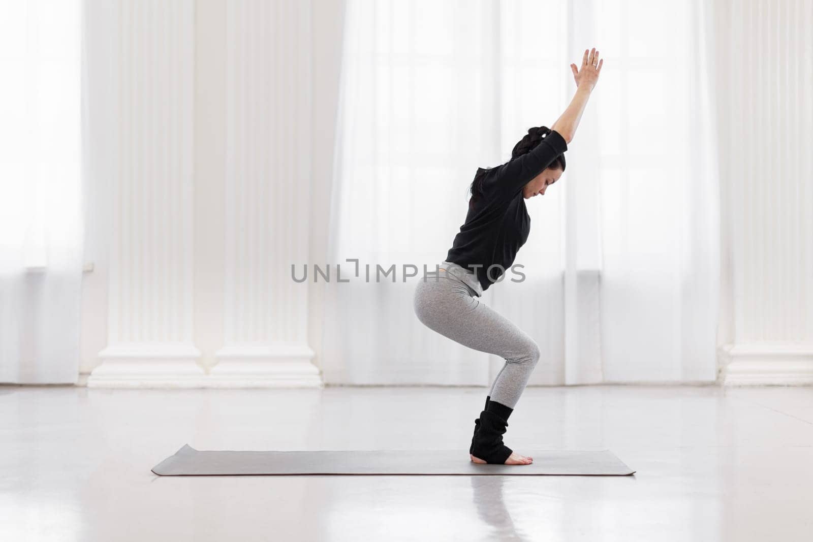Side view of young mixed race female yoga instructor doing utkatasana on mat in her spacious living room. Corrects minor defects in legs strengthens ankles promotes even development of leg muscles by apavlin
