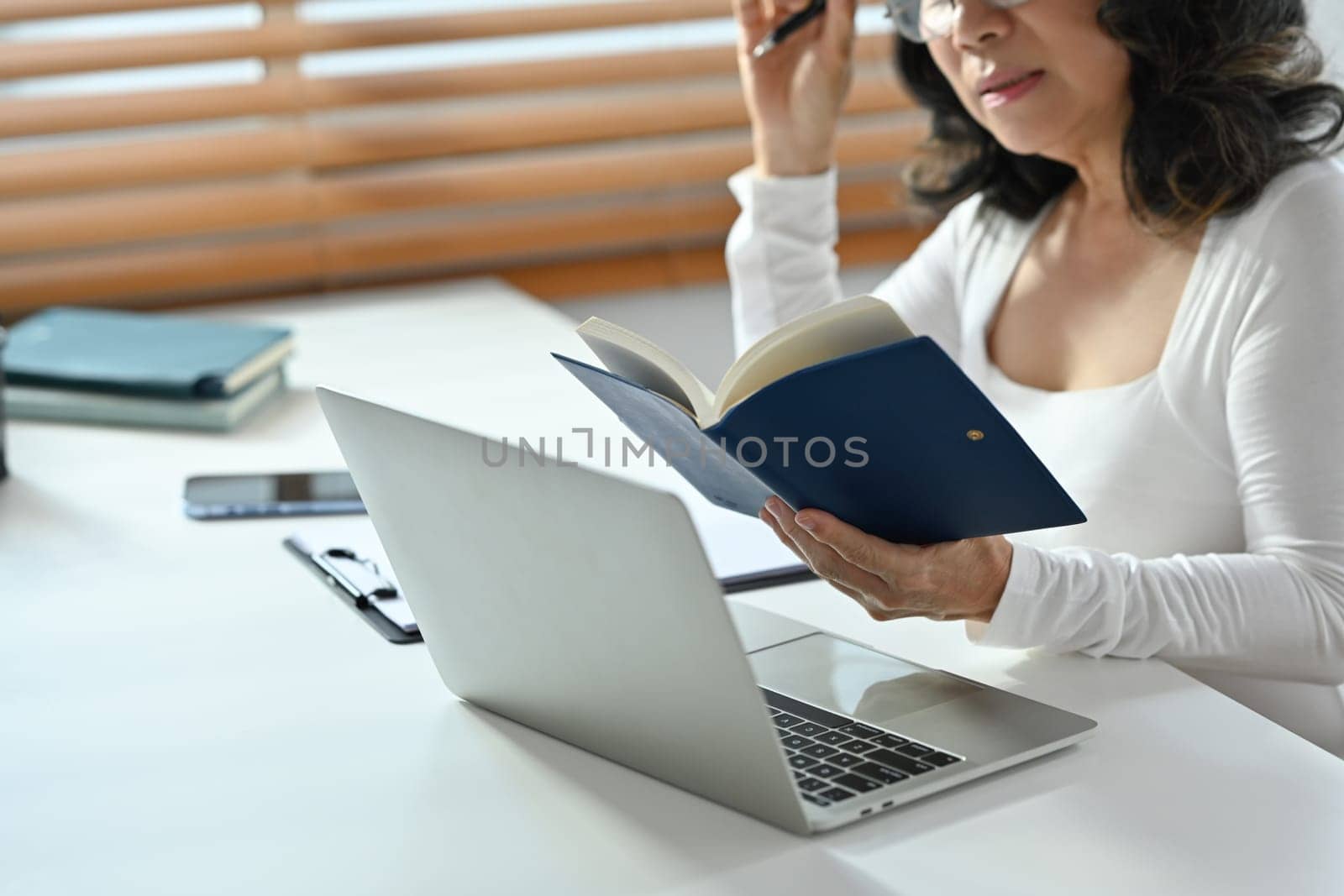 Cropped shot of middle aged woman checking working schedule plan, sitting in front of laptop at working desk by prathanchorruangsak