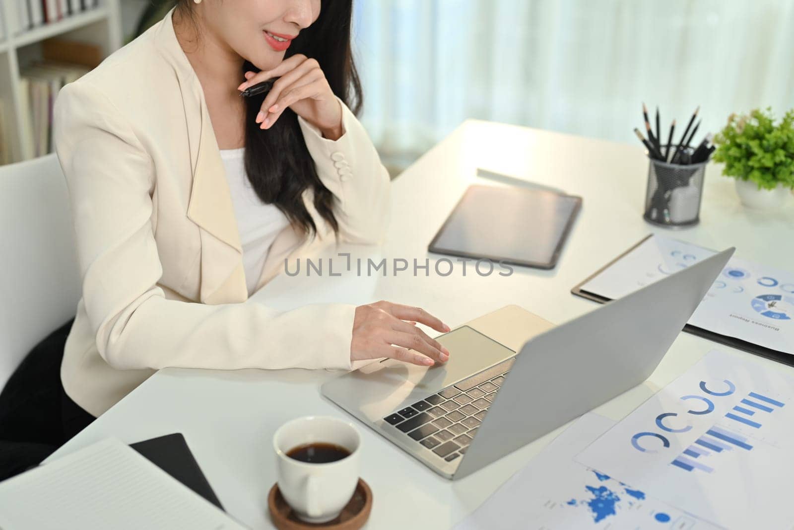 Focused female financial analyst checking online data, working with statistics at white office desk by prathanchorruangsak