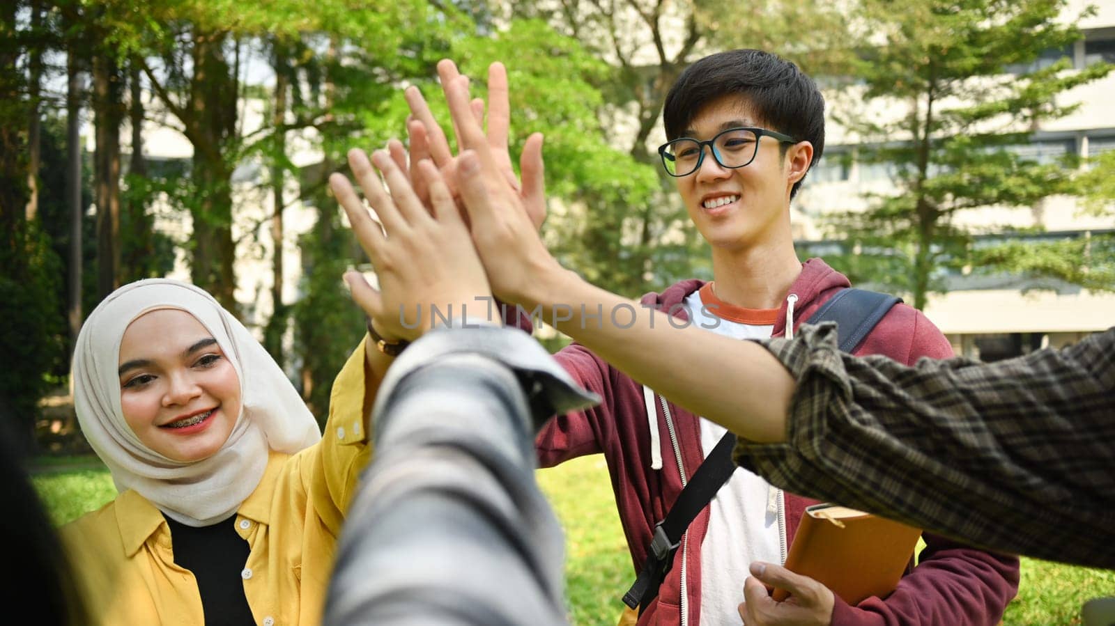 Happy university friends are giving high five, celebrating together. University, youth lifestyle and friendship concept by prathanchorruangsak
