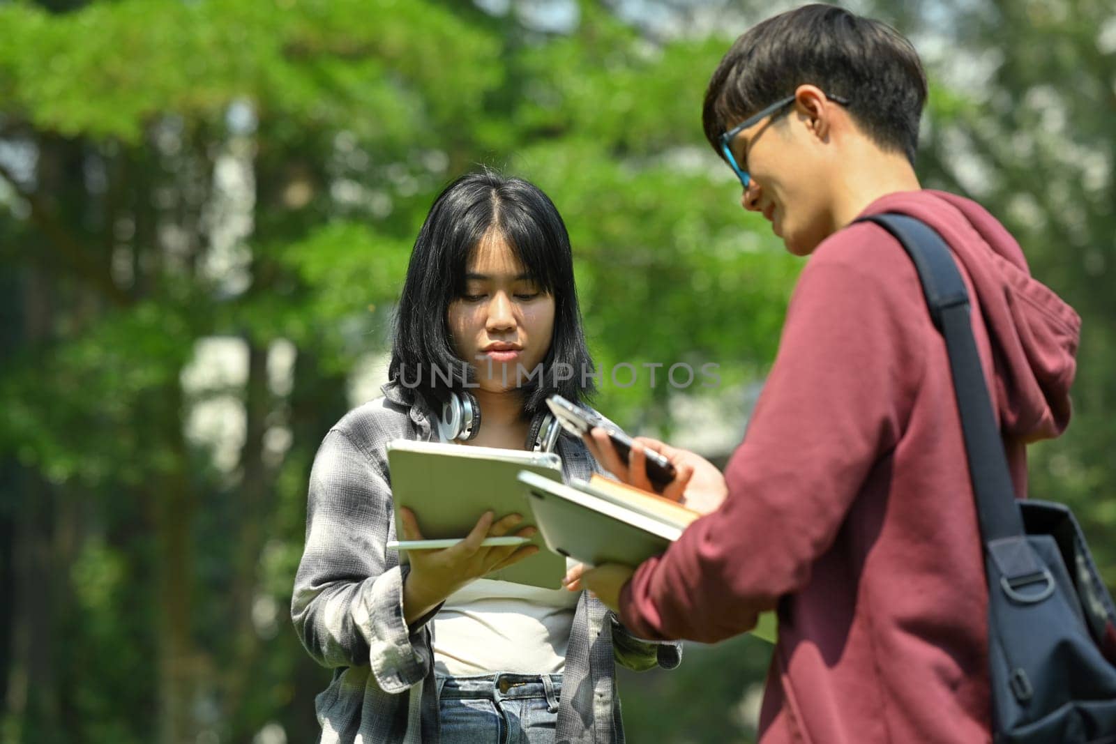 Two asian students are talking to each other after classes while walking outdoors in university. Education and youth lifestyle concept.