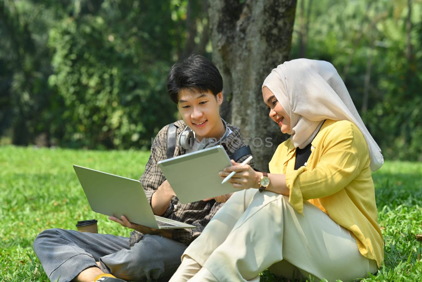 Smiling muslim university student and her friend working on laptop at green lawn in university. Education and technology concept by prathanchorruangsak