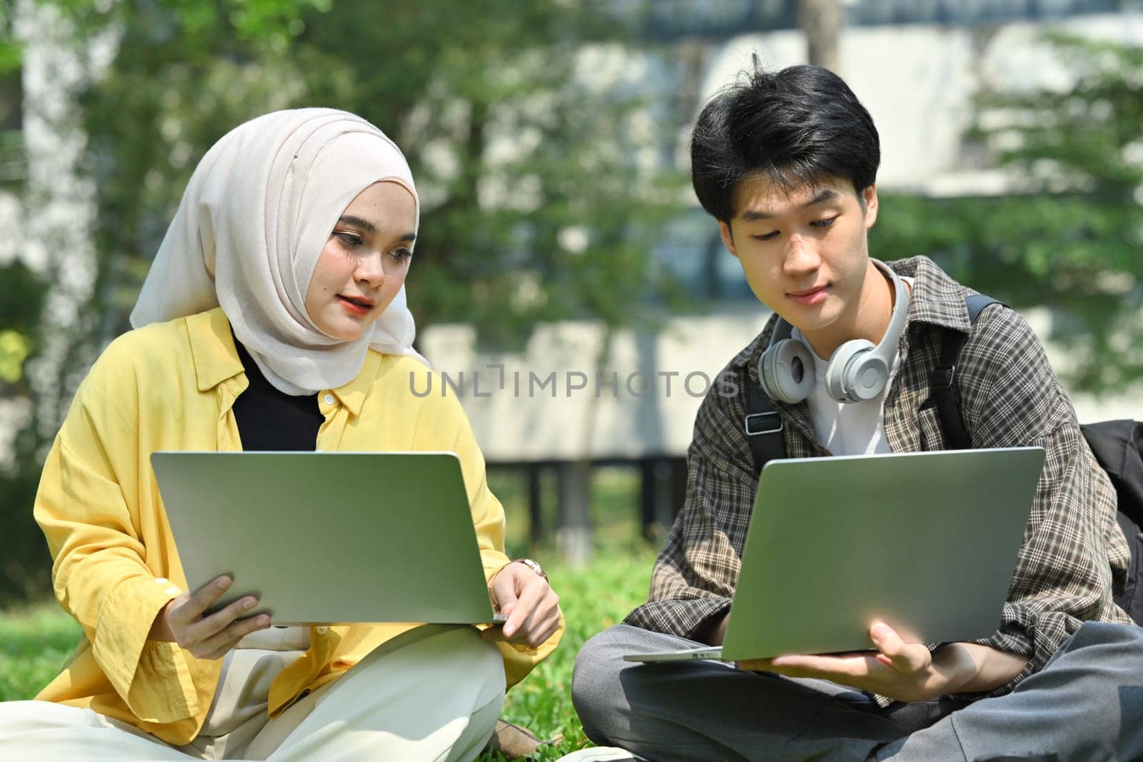 Female Muslim college student and classmates making research, working on group project on laptop at outdoor.