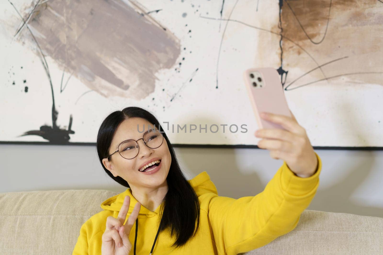 Asian student takes selfie with smartphone, utilizing the latest in mobile photography and communication technology. With glasses on, she captures self-portrait to share on social media or with friends online. High quality photo