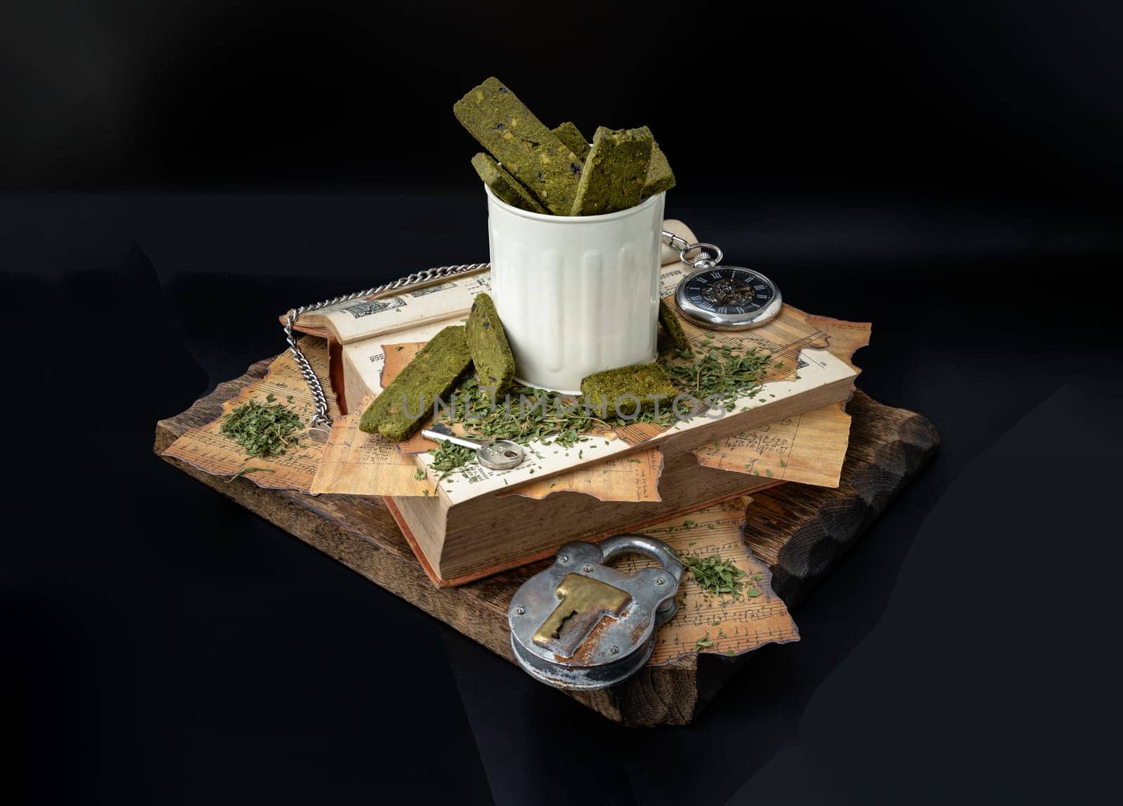 Bangkok, Thailand - Mar 17, 2023 : Homemade Cannabis Snack Sticks in the steel cup are on the Old Song Book with the Analog Pocket Watch and Vintage Iron Padlock on old wooden plank with dark backgroud. The Concept of Relaxation and the Happiness, Vintage style, Space for text.