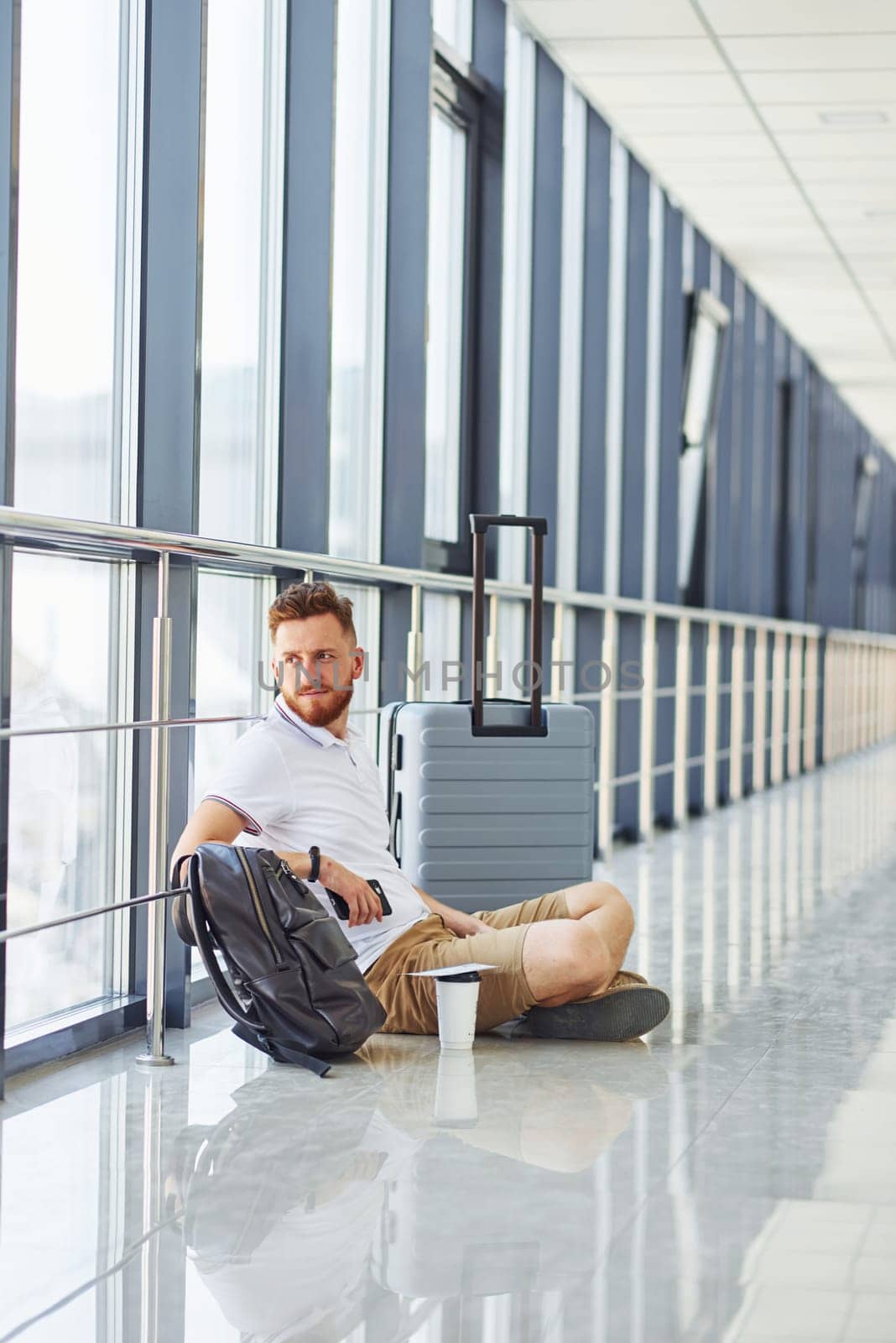 Man sitting on the ground. Young traveler is on the entrance hall in the airport.