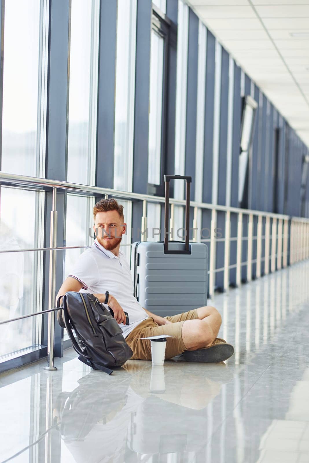 Man sitting on the ground. Young traveler is on the entrance hall in the airport.
