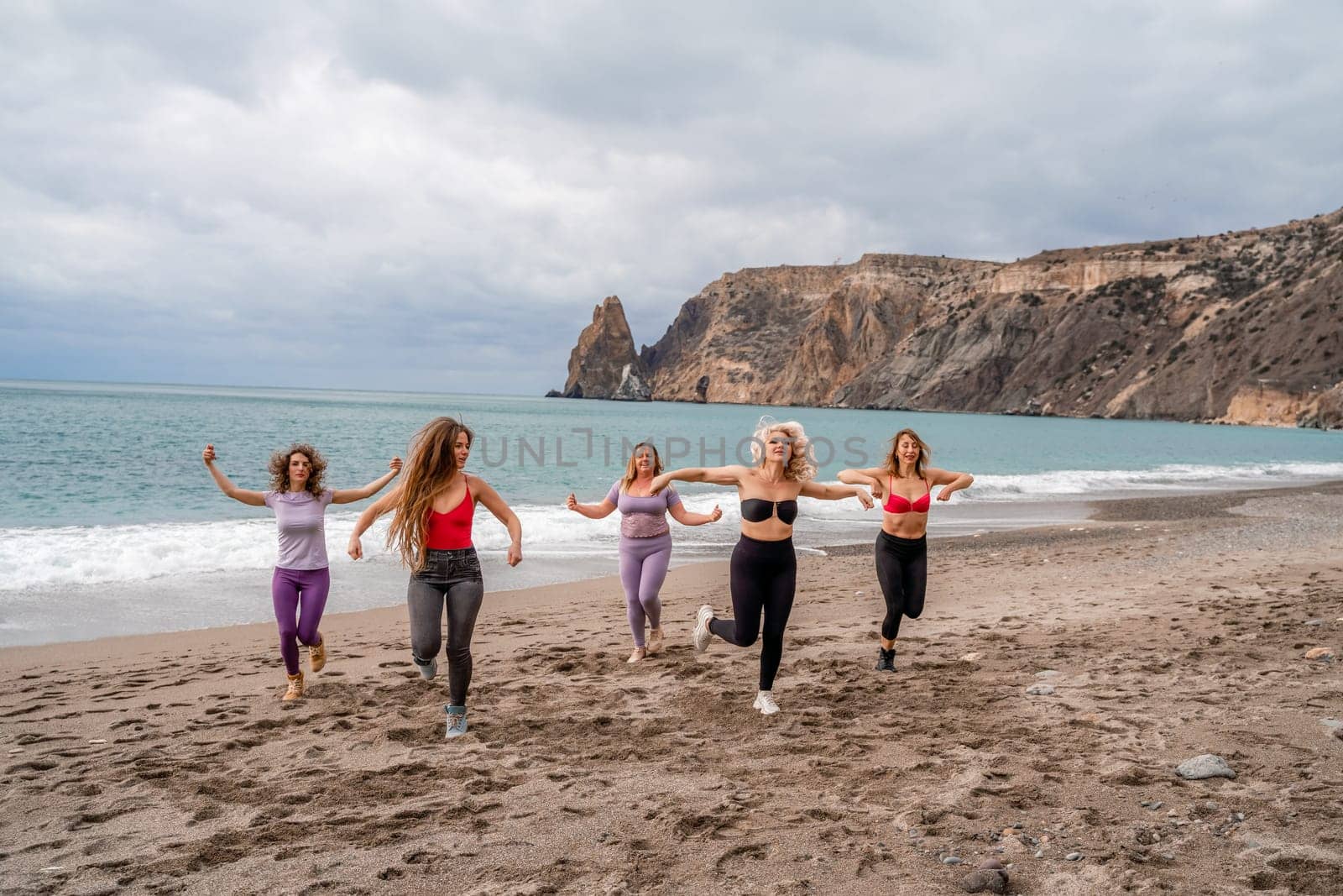 A group of five female friends are doing exercises on the beach. Beach holiday concept, healthy lifestyle by Matiunina