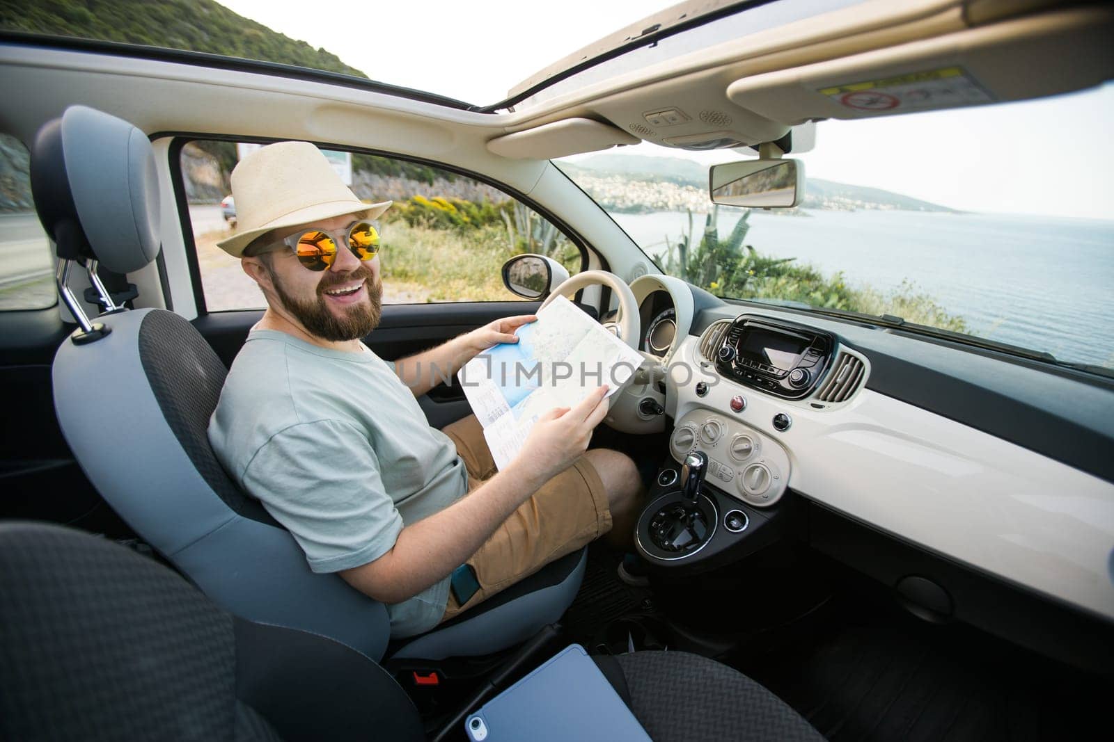 Hipster man looking on location navigation map in car, tourist traveler driving and hold in male hands europe cartography, view and plan tourist way road, trip in transportation cabriolet auto by Satura86