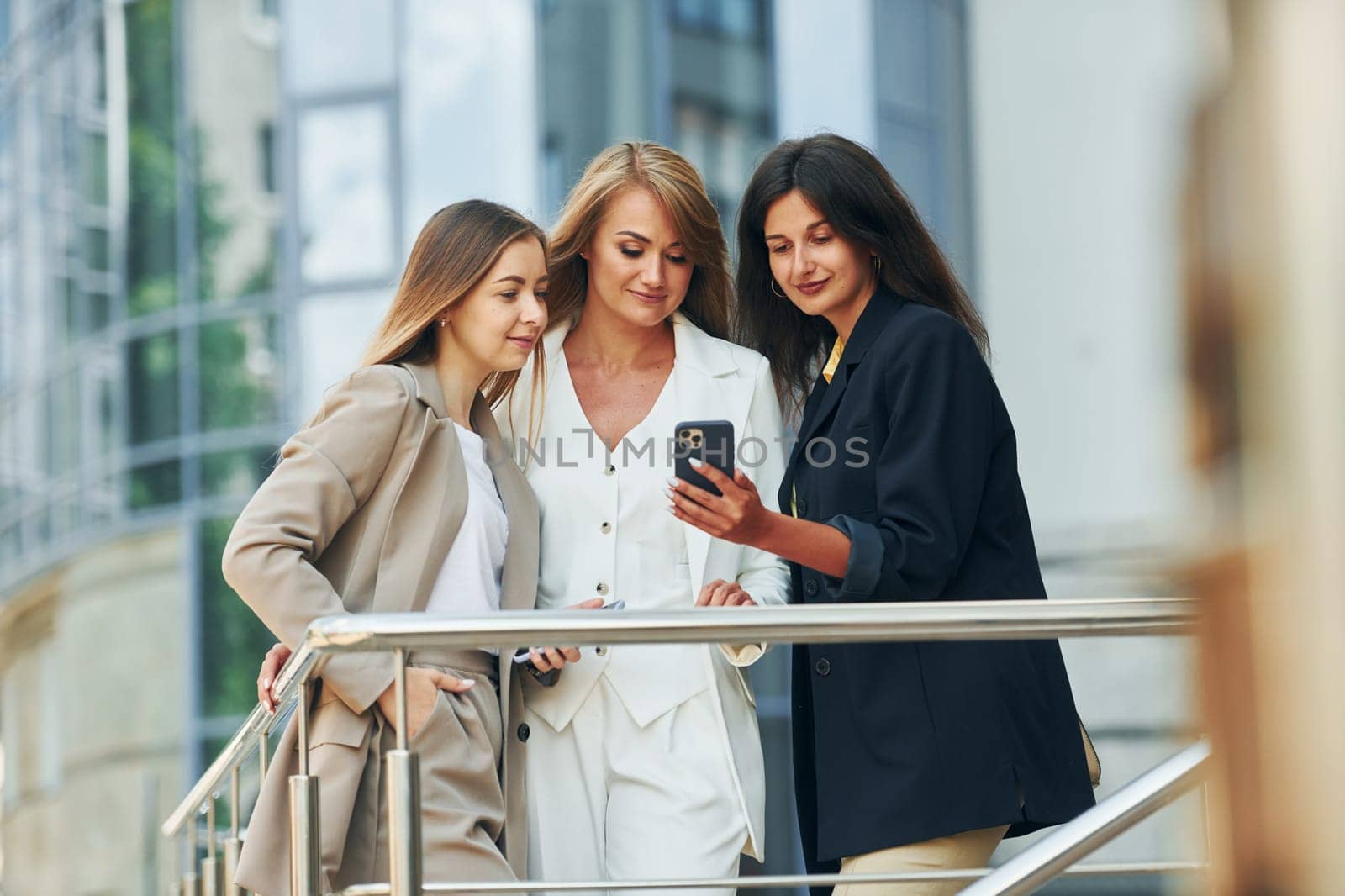 Using phone. Women in formal wear is outdoors in the city together.
