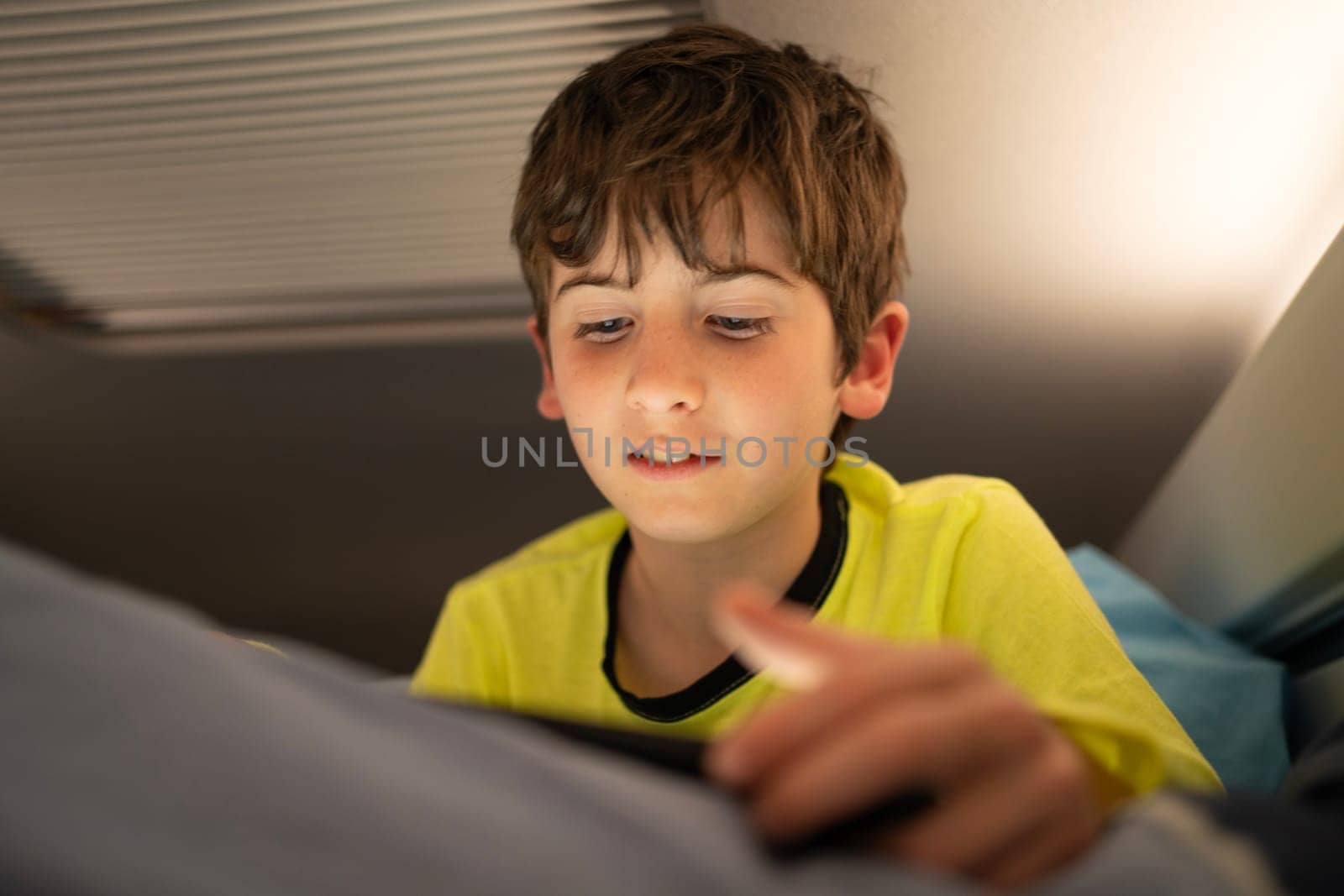 Young boy with tablet in motorhome on road trip vacations. Kid enjoying in camper indoor at night.Active family holidays by papatonic