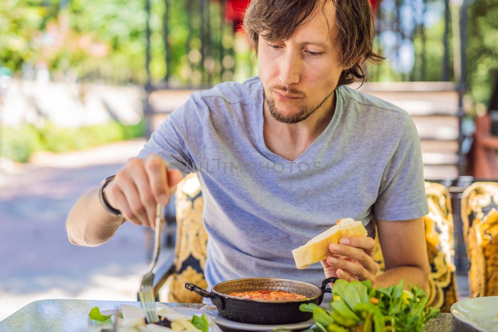 man tourist eat Turkish breakfast. Turkish breakfast table. Pastries, vegetables, greens, olives, cheeses, fried eggs, spices, jams, honey, tea in copper pot and tulip glasses, wide composition by galitskaya