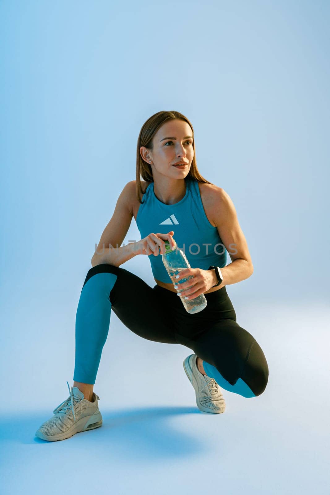 Woman drinking water from bottle while workout and doing sport exercises on studio background