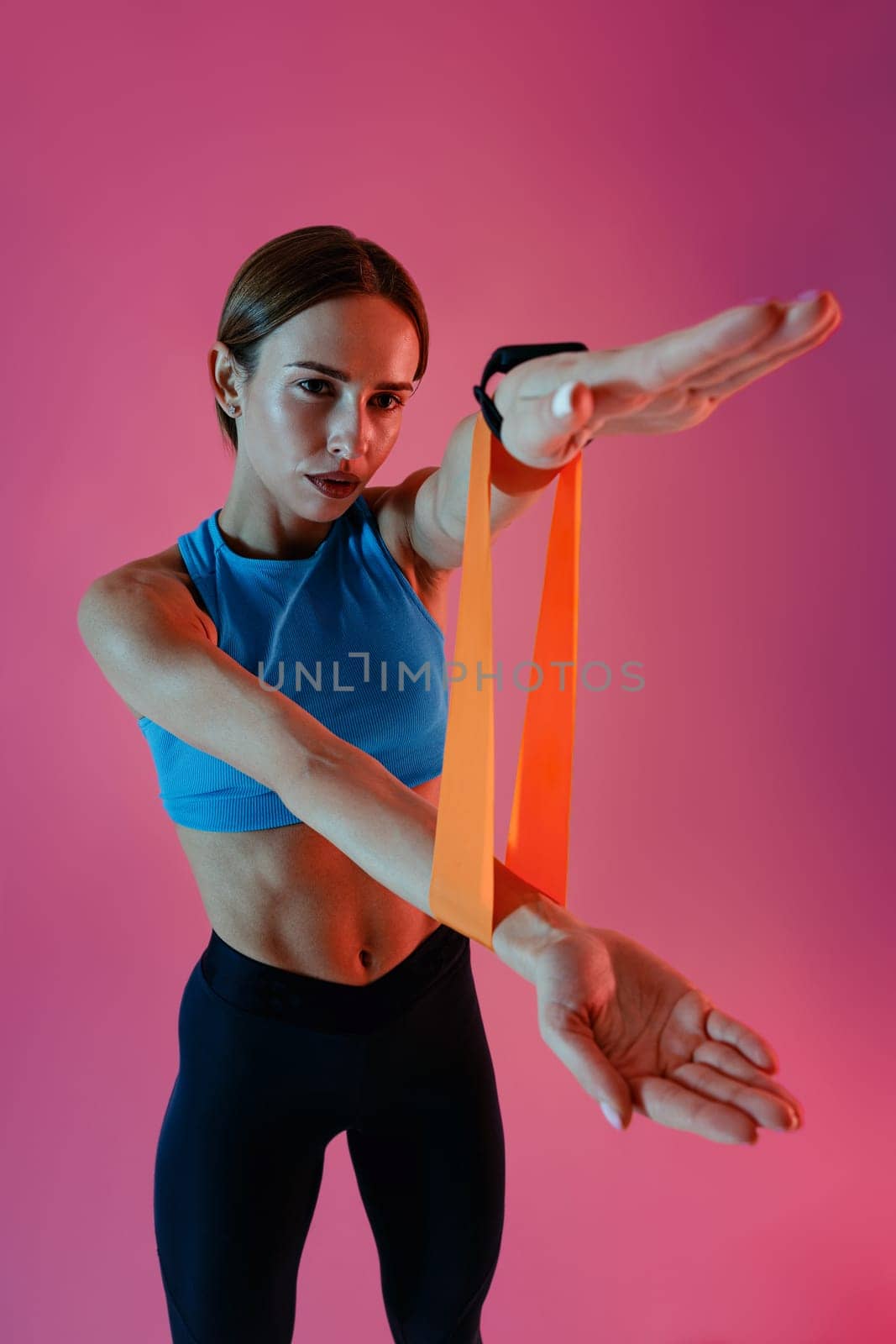 Sports woman with her hands stretches rubber elastic band for training on studio background by Yaroslav_astakhov
