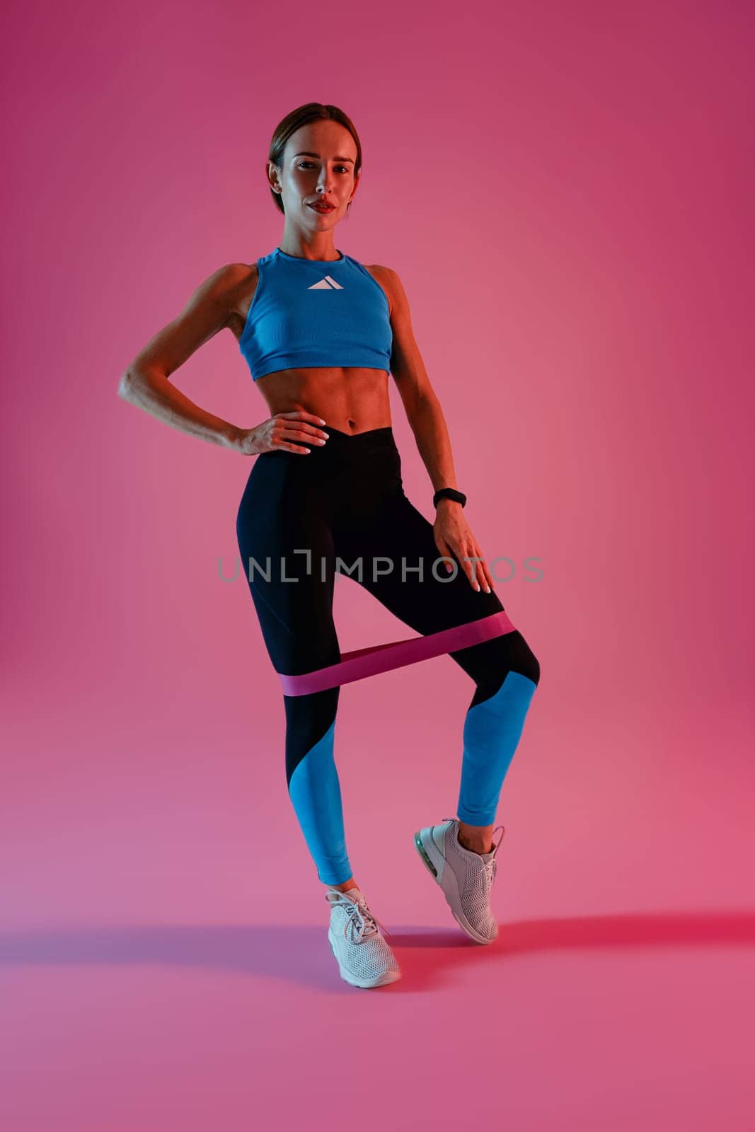 Athletic woman trains legs with fitness elastic band on studio background. High quality photo