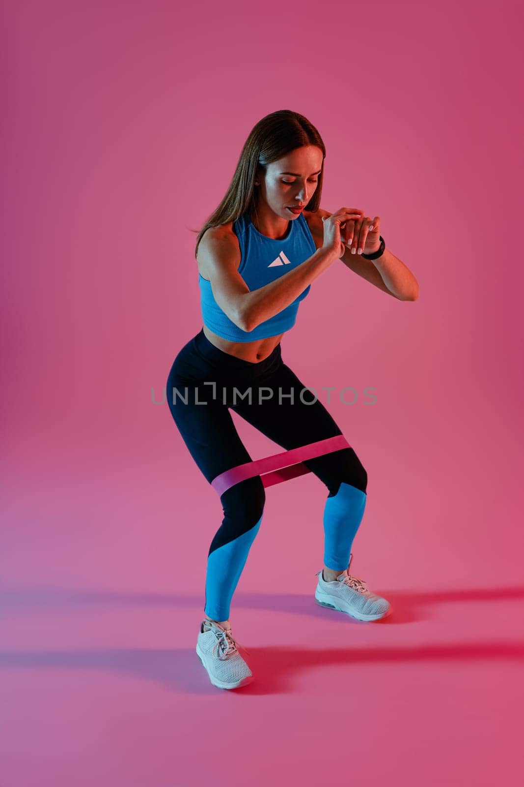 Fitness woman standing and stretching elastic band with legs on studio background by Yaroslav_astakhov