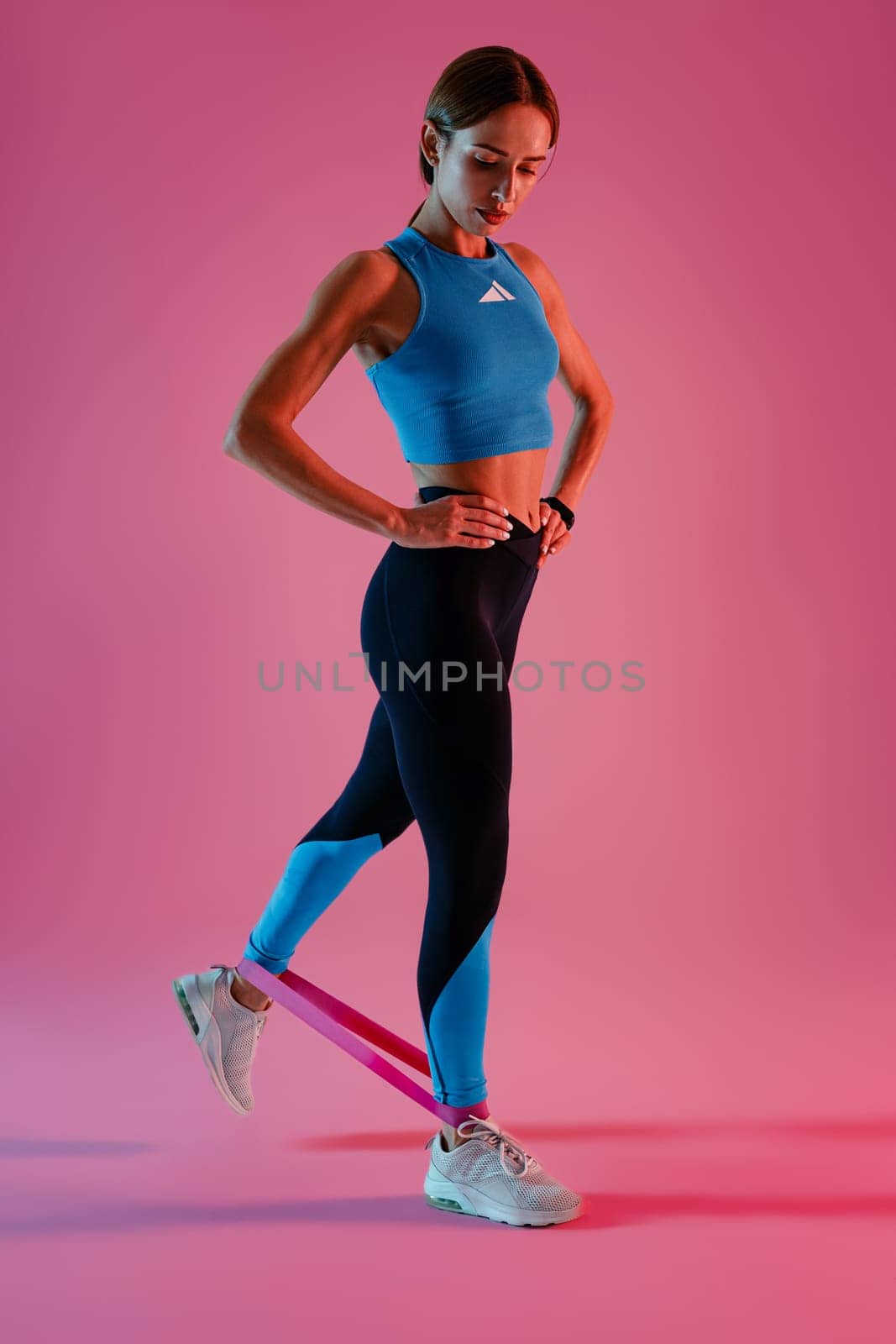 Strong woman in sportswear performs fitness exercises with resistance band on studio background by Yaroslav_astakhov