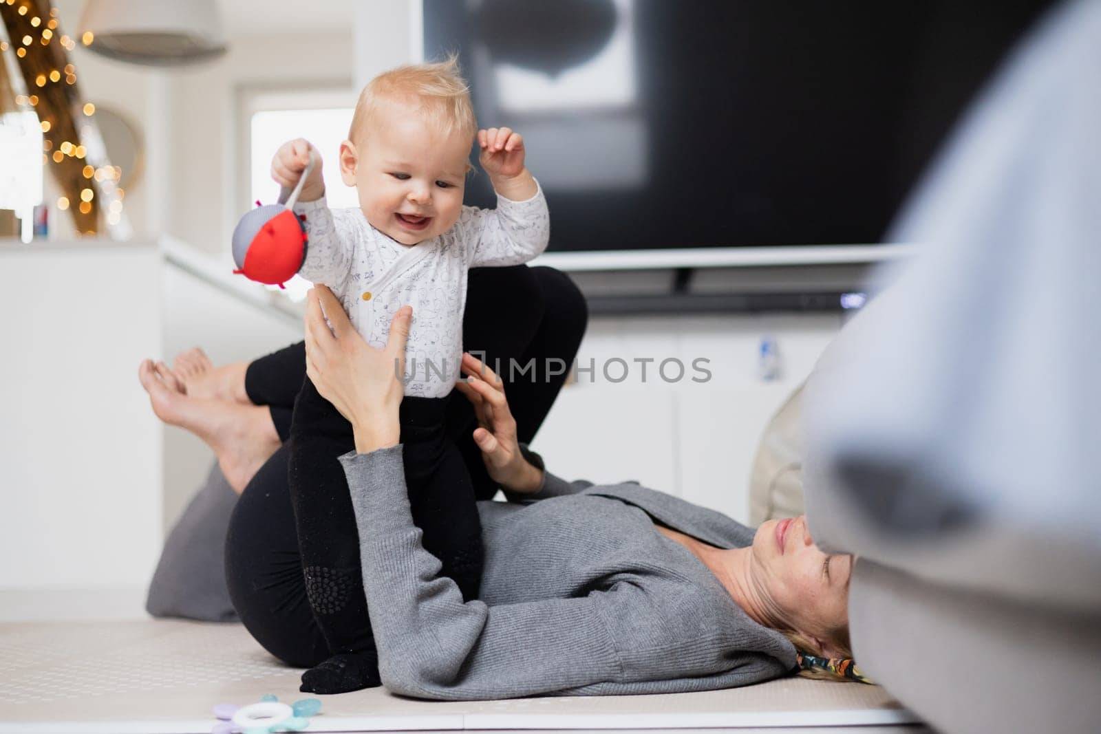 Happy family moments. Mother lying comfortably on children's mat playing with her baby boy watching and suppervising his first steps. Positive human emotions, feelings, joy