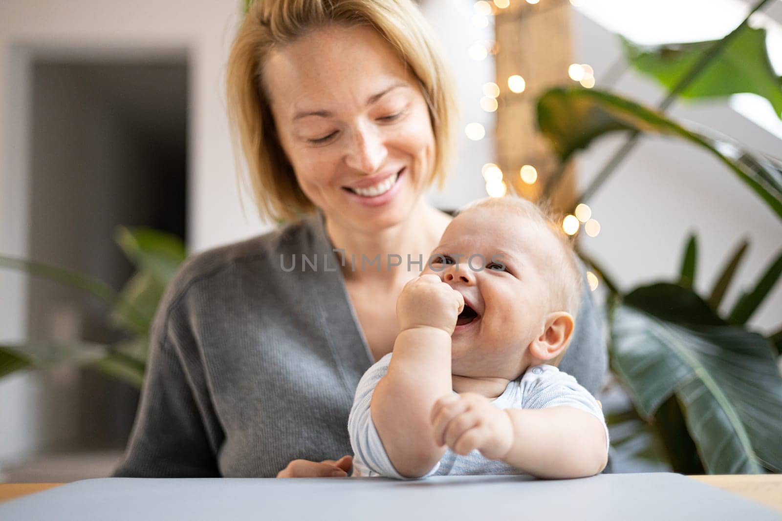 Portrait of young mother cuddling her adorable little child while sitting at the table at home. Sensory stimulation for baby development.