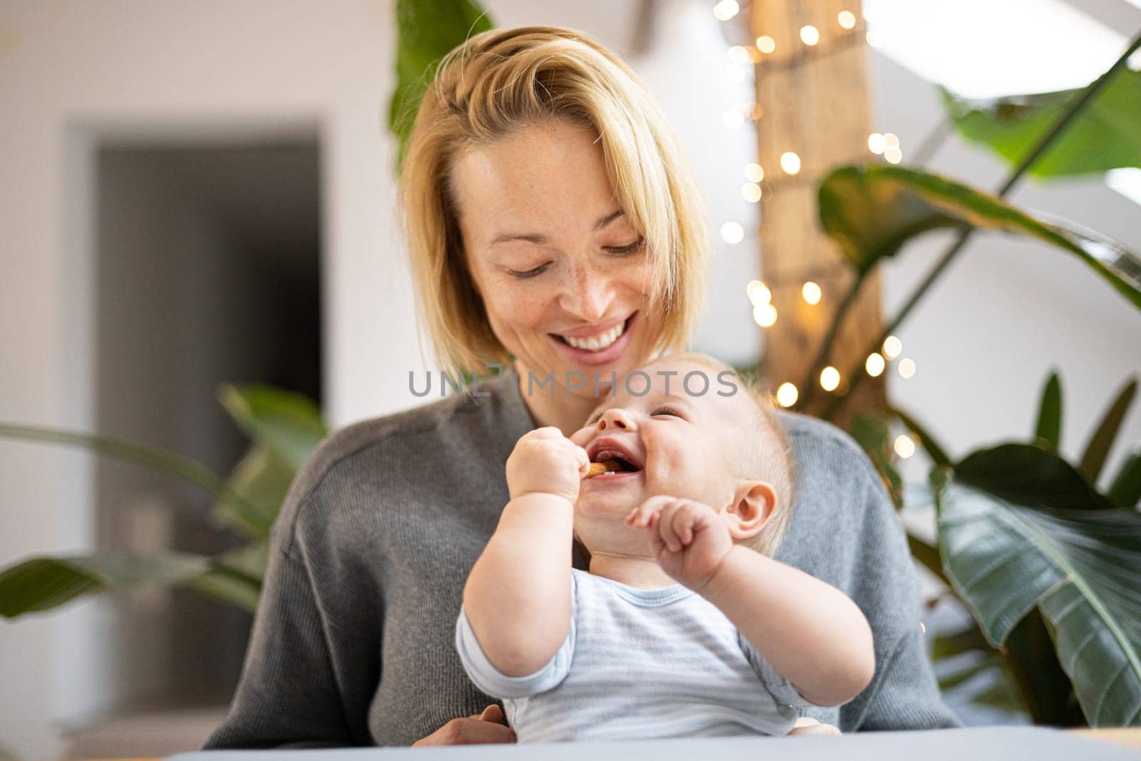 Portrait of young mother cuddling her adorable little child while sitting at the table at home. Sensory stimulation for baby development by kasto