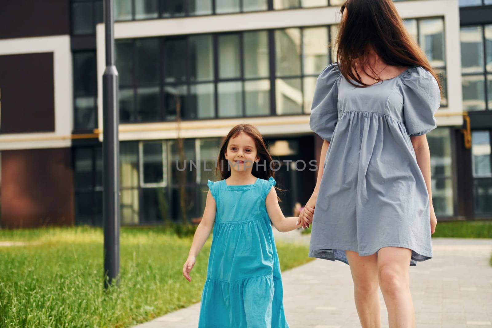 Young mother with her little daughter walking near the buildings.